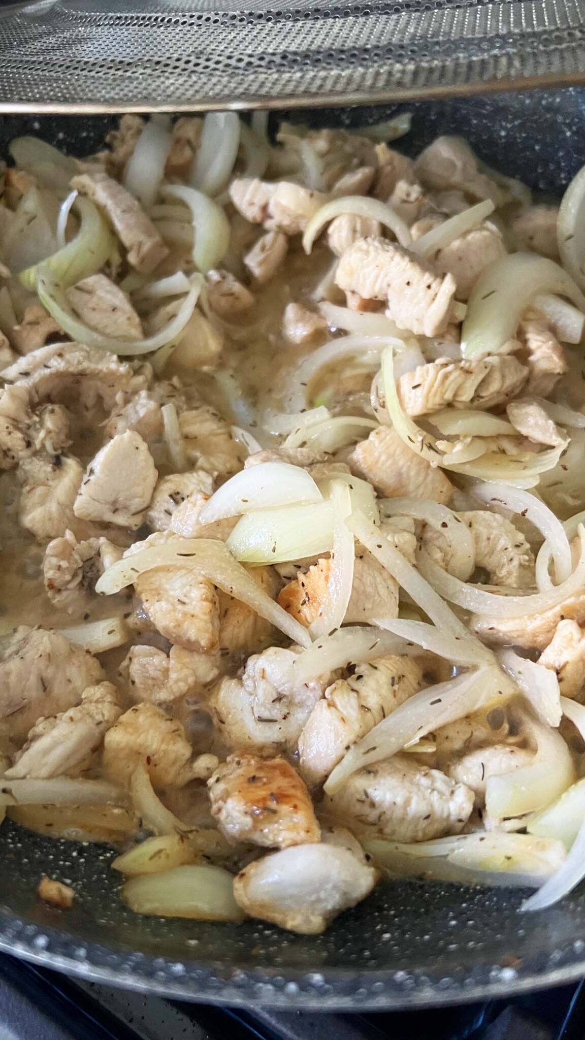Chicken and onions in a grey skillet.