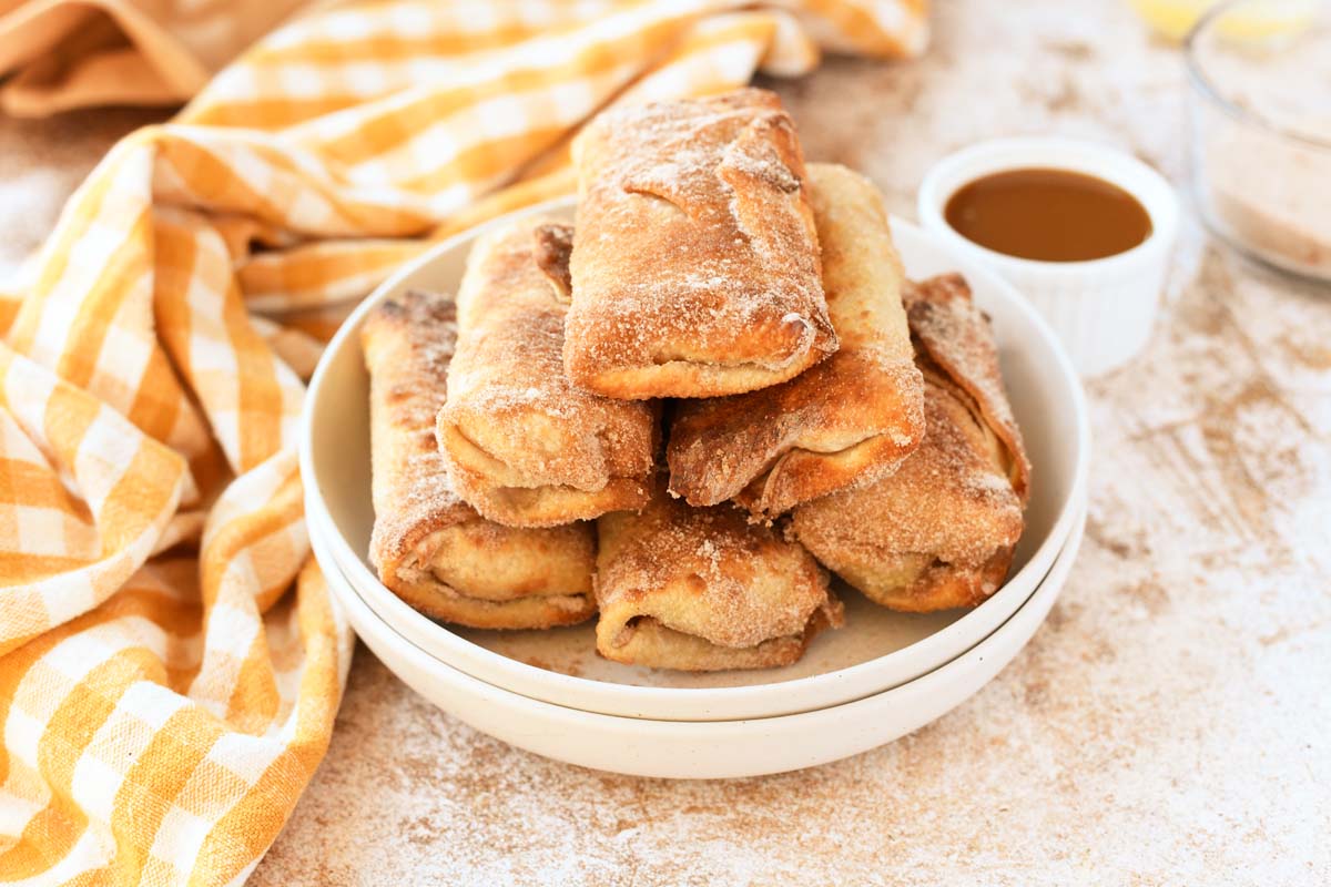 A white plate with a yellow checked napkin and apple pie egg rolls.