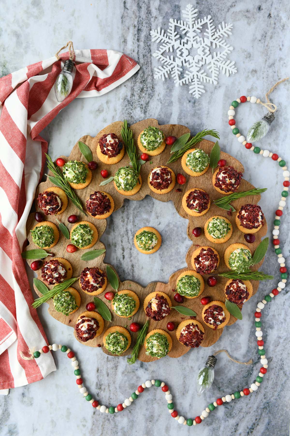 A cheeseball wreath on a grey surface with Christmas ornaments.