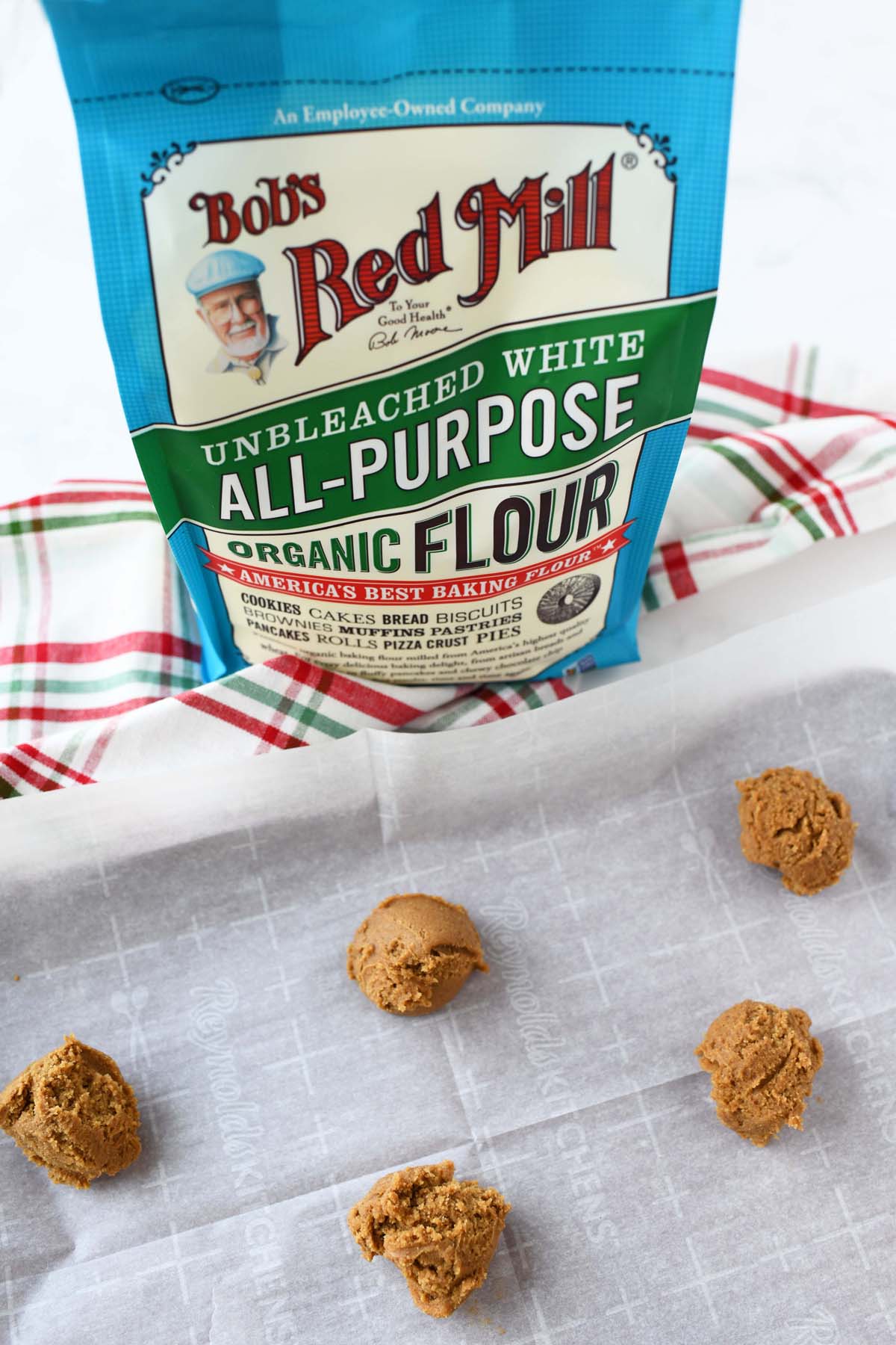 Bobs red mill organic flour with unbaked cookie dough balls on a baking sheet.