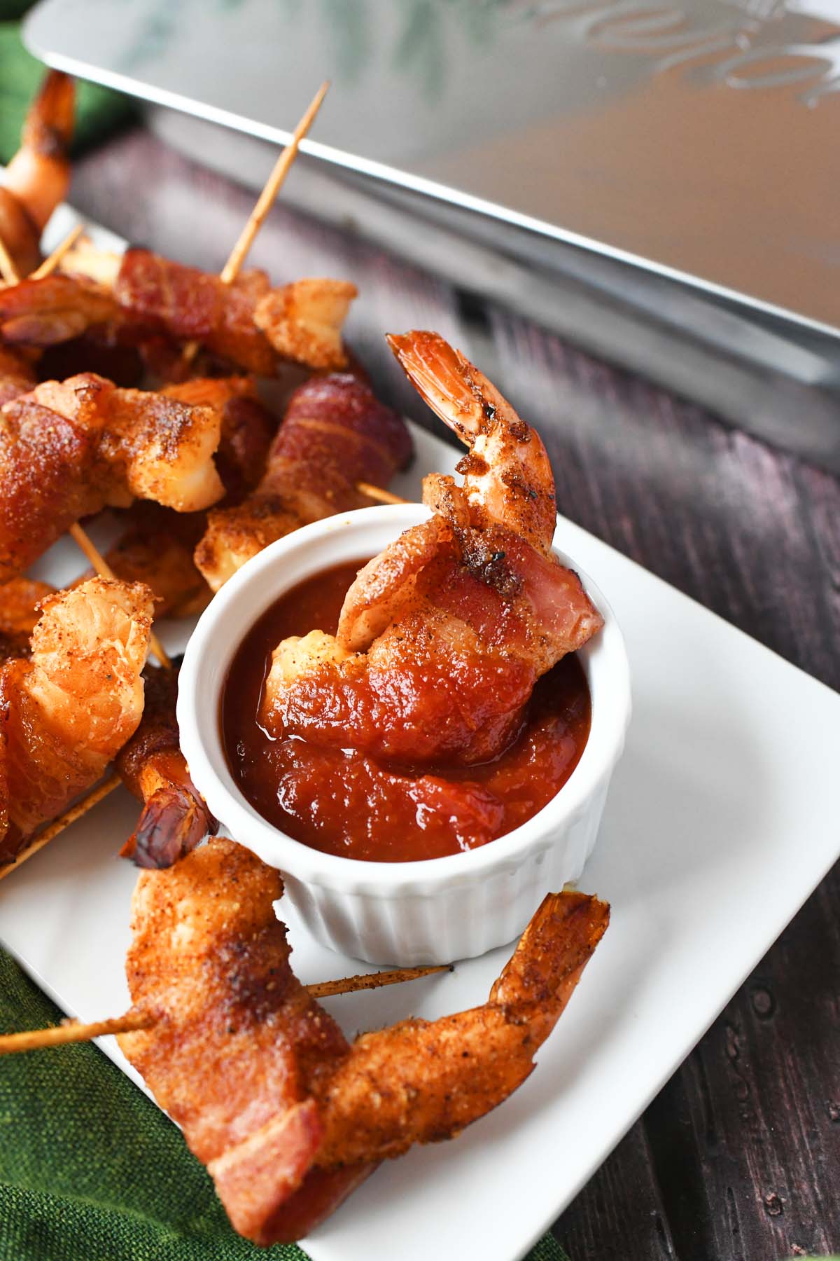 A bacon wrapped shrimp dunked in chili sauce in a white ramekin.