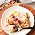 A slice of orange cranberry bread pudding on a small, white plate.