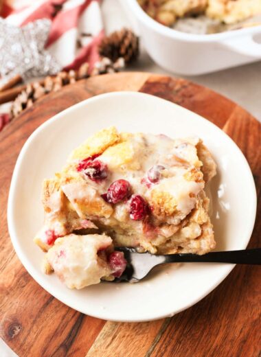 A slice of orange cranberry bread pudding on a small, white plate.