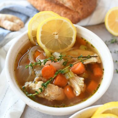 A white bowl of ginger chicken noodle soup with lemon and thyme.