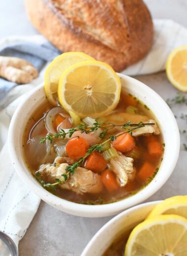 A white bowl of ginger chicken noodle soup with lemon and thyme.
