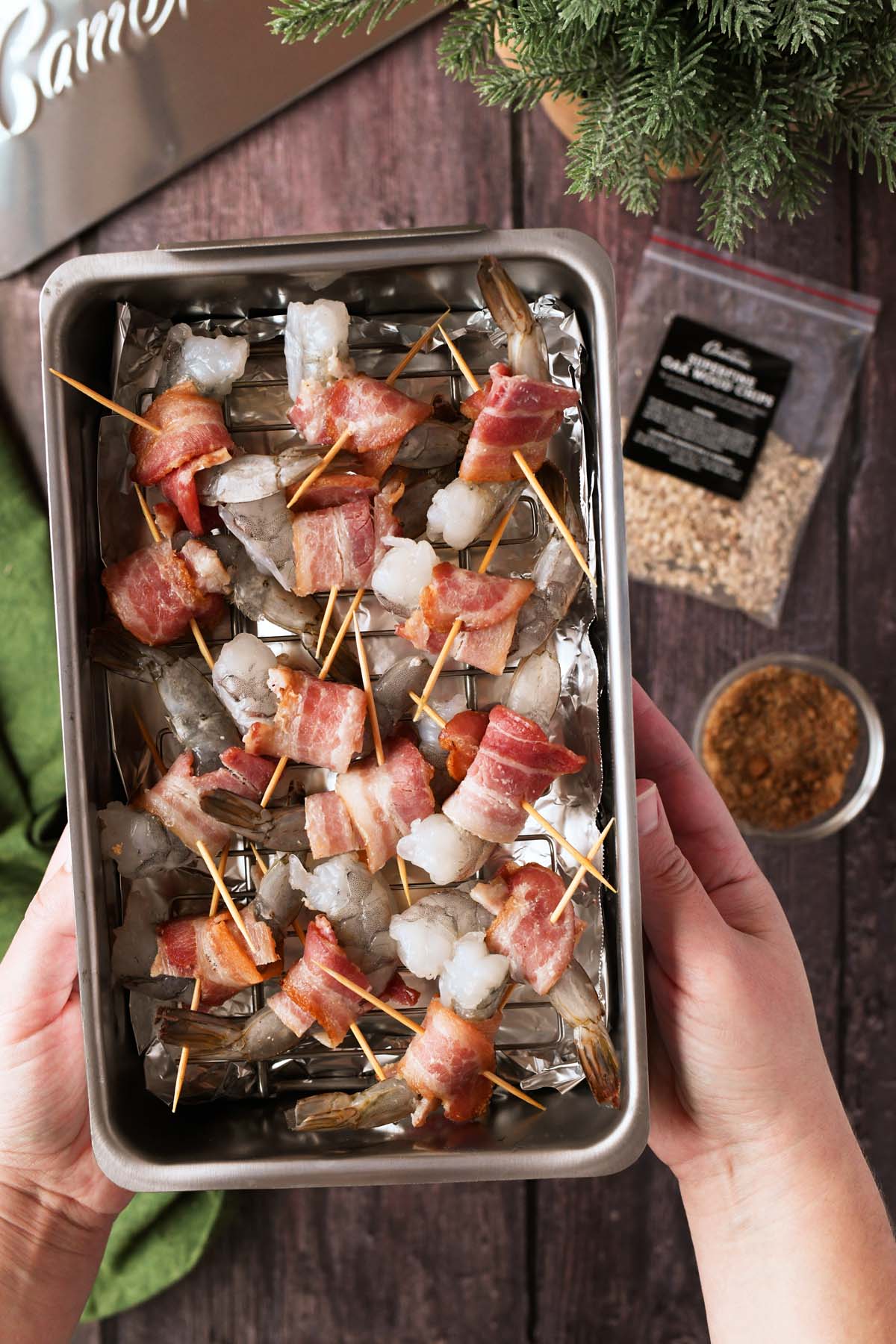A smoker filled with uncooked bacon wrapped shrimp in white hands.