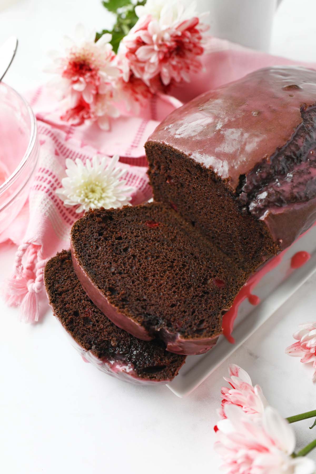 A chocolate cherry cake sliced near a pink napkin with fresh flowers.