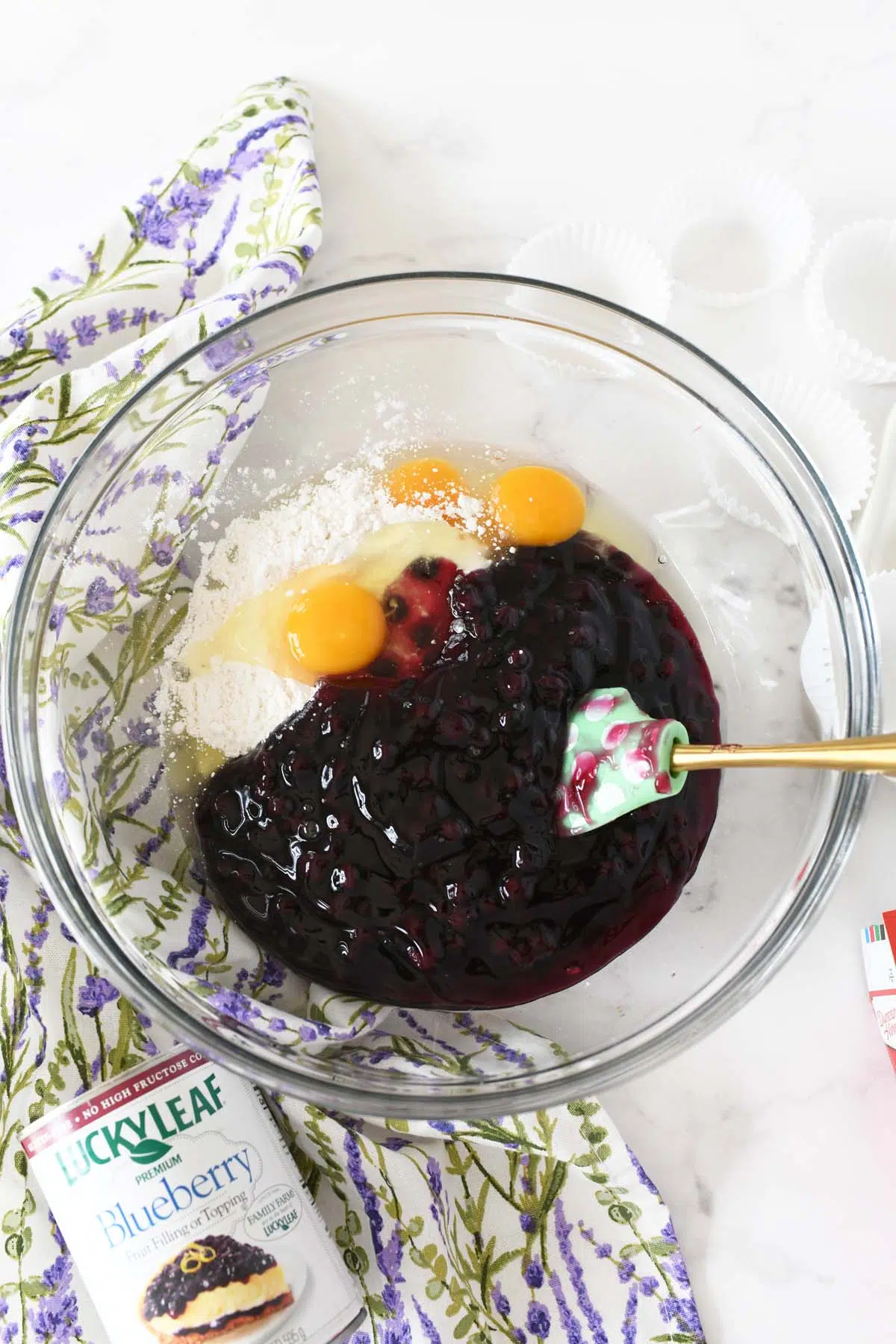 A mixing bowl with white cake mix, blueberries, and eggs.