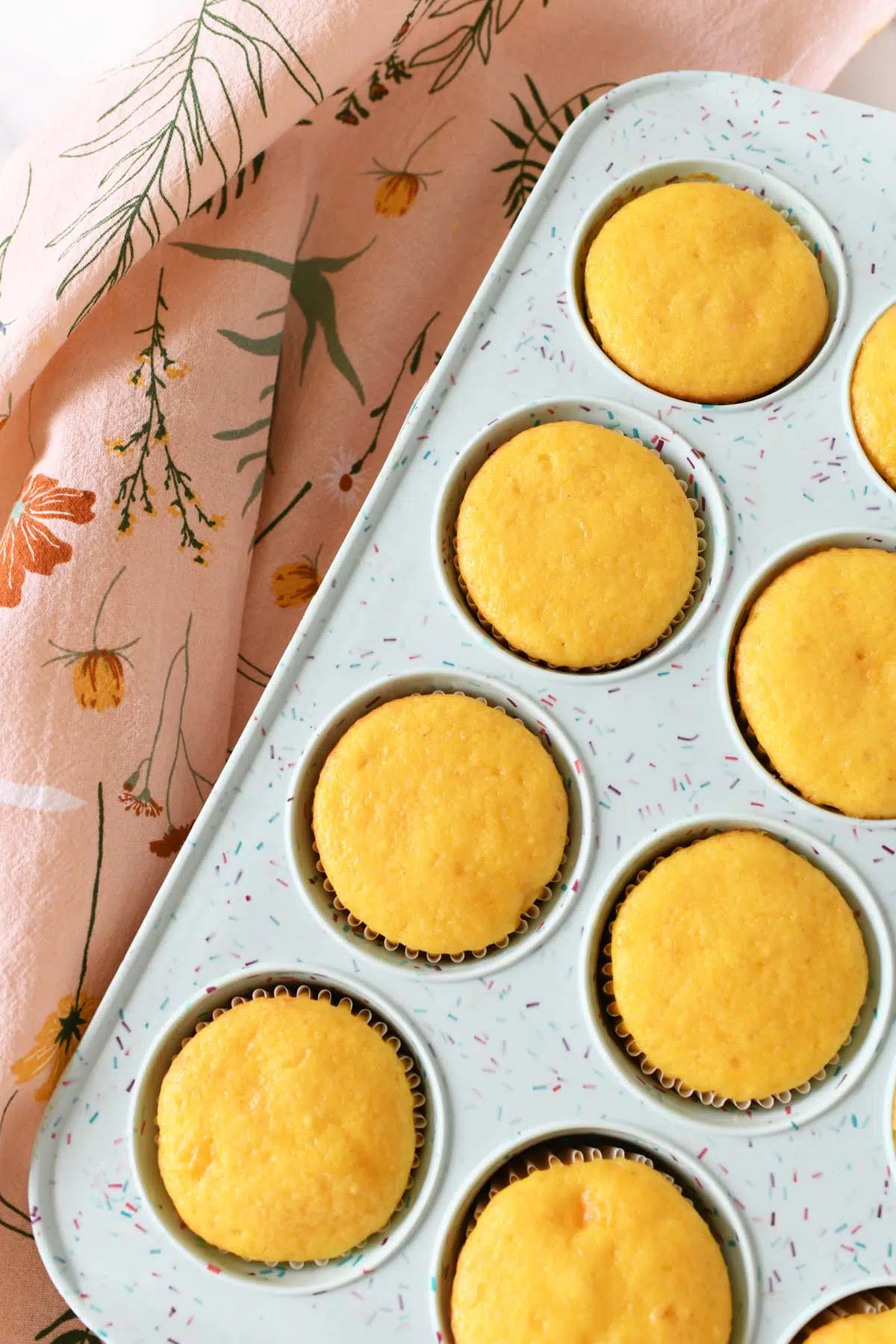 Yellow peach cupcakes in a blue muffin tin with a pink, floral napkin.
