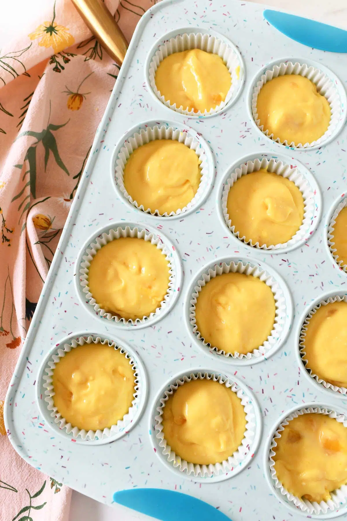 Yellow cupcake batter in a blue muffin tin.