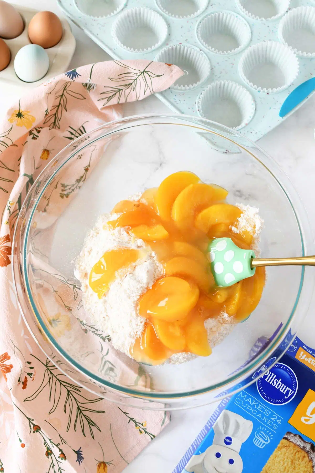 Peach pie filling and cake mix in a glass bowl with a green spatula.