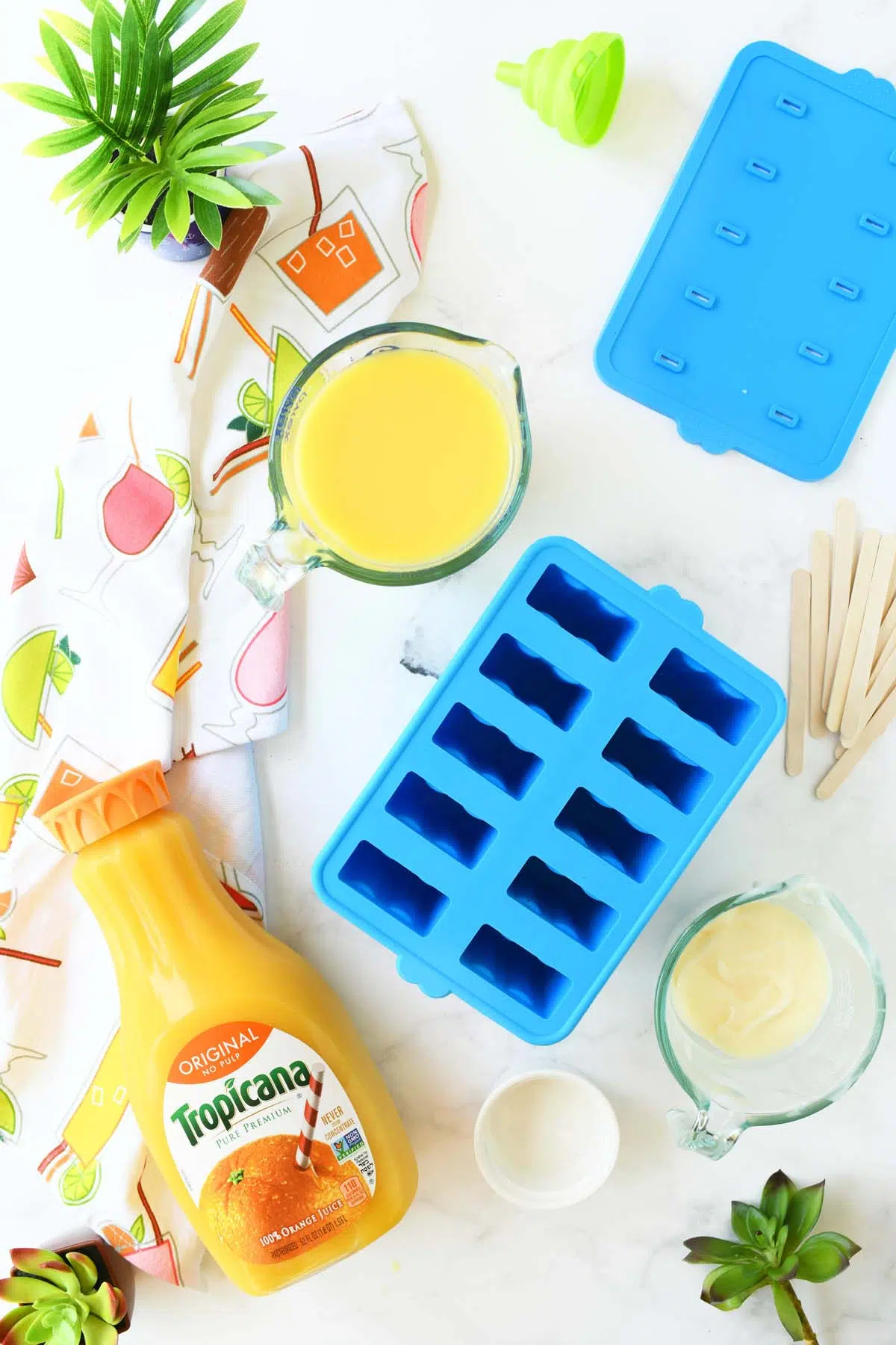 Blue ice pop mold with oj pops ingredients on a white table.