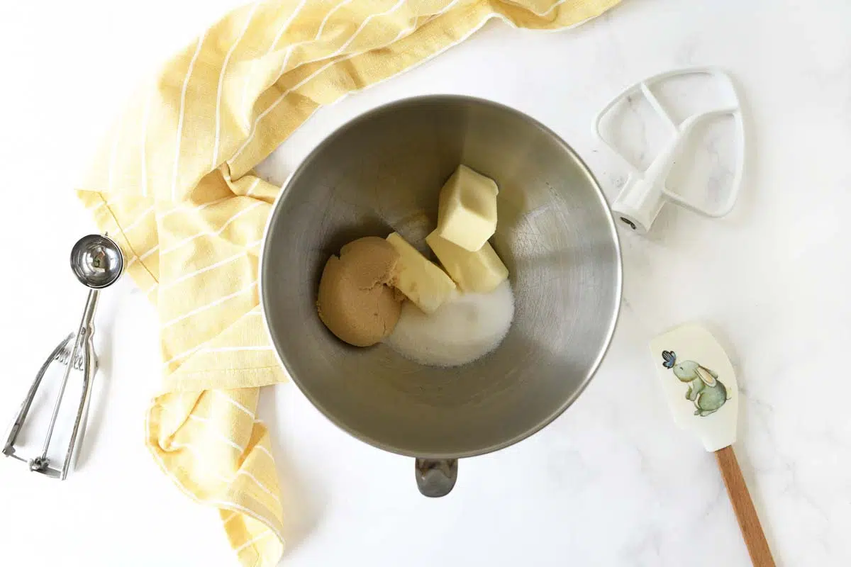 Butter and Sugar in a stand mixer with a yellow napkin and cookie scoop nearby.