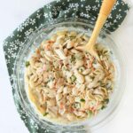 Creamy Italian dressing crab pasta salad in a glass bowl with a wooden spoon and green napkin.