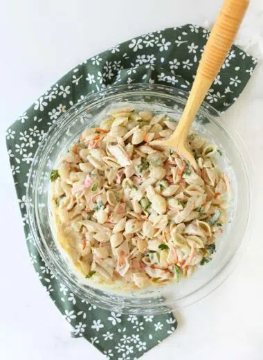 Creamy Italian dressing crab pasta salad in a glass bowl with a wooden spoon and green napkin.
