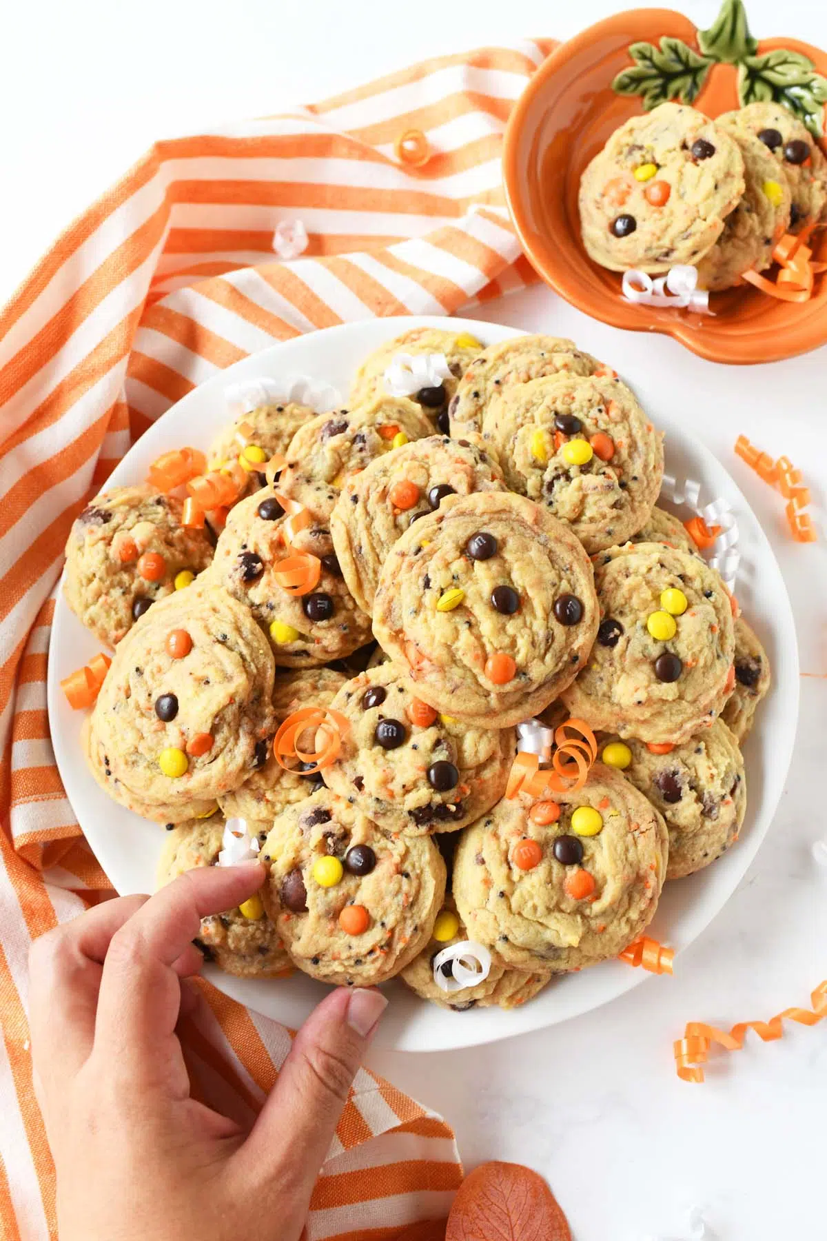 A hand grabbing orange, yellow, and brown cookies near an orange striped napkin.