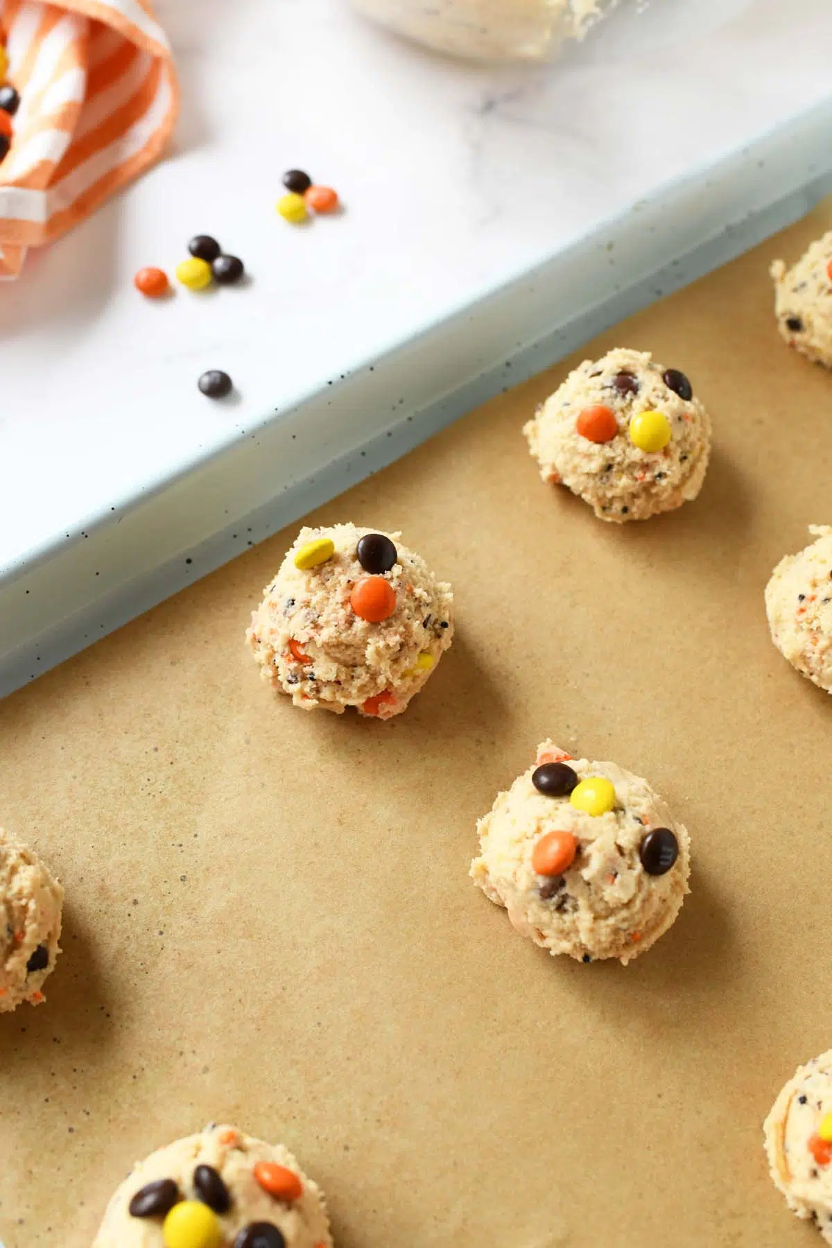 Orange, yellow, and brown cookie dough balls on parchment paper.