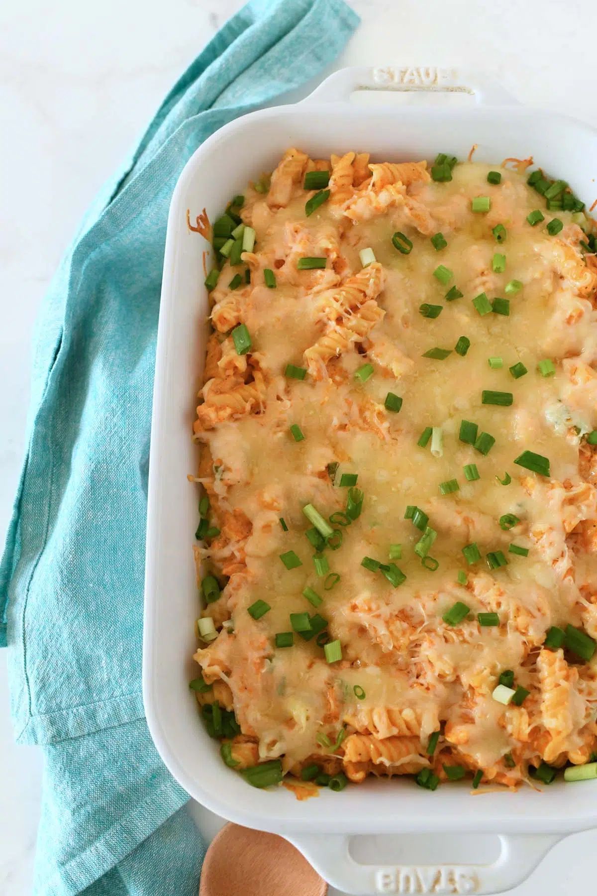 Baked buffalo chicken pasta with green onions near a blue napkin.