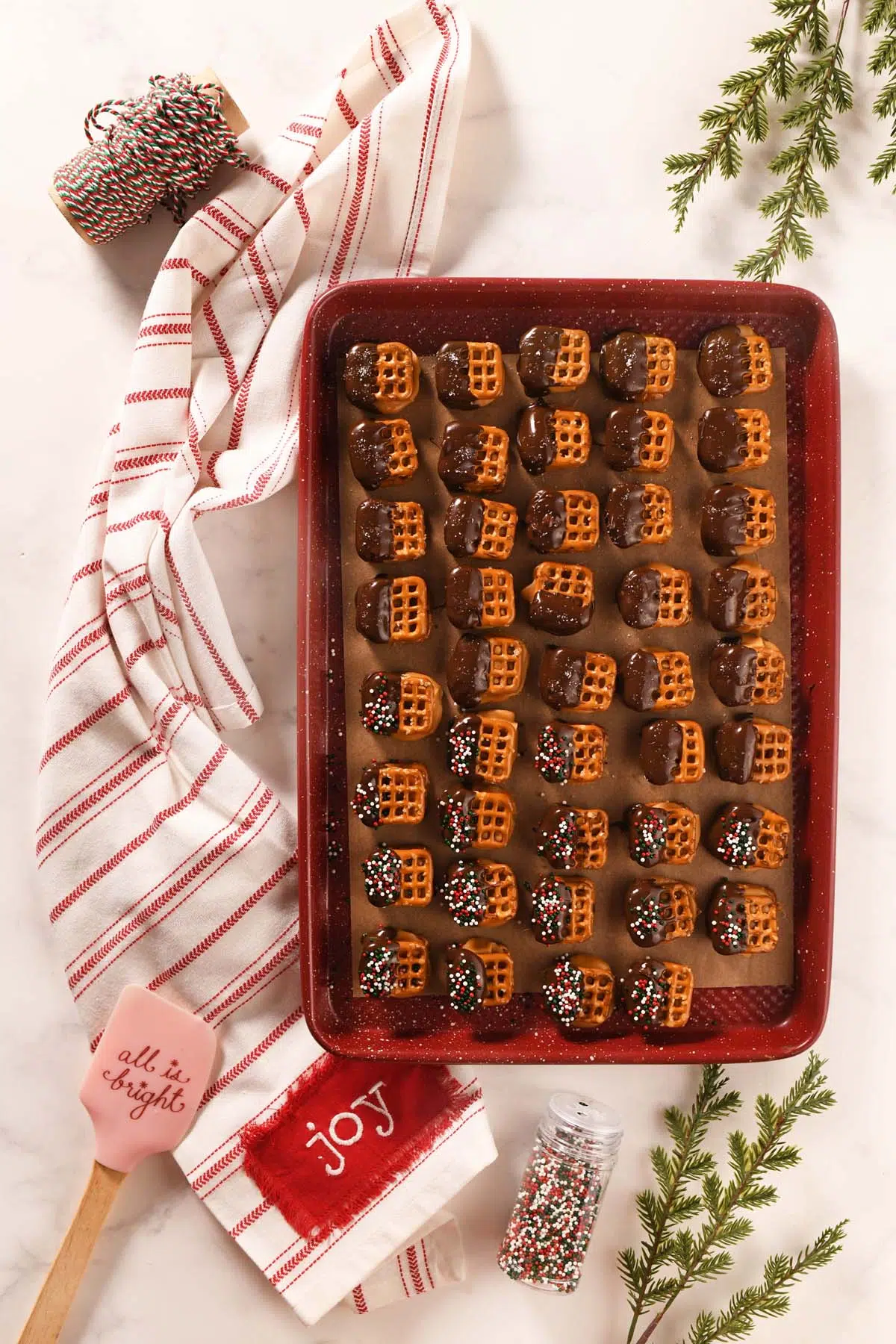 Salted caramel pretzels on a red baking sheet with holiday napkins.