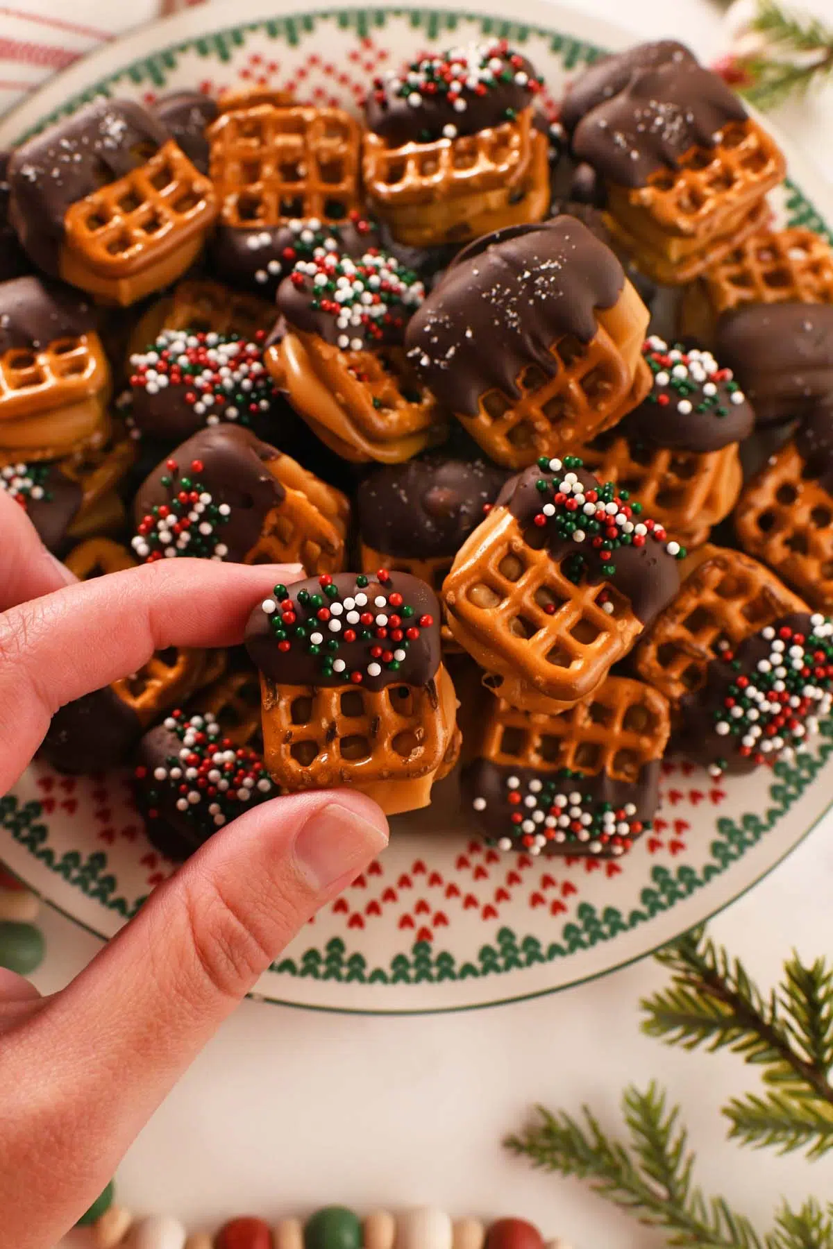 A white hand grabbing a small, chocolate caramel mini pretzel bite.