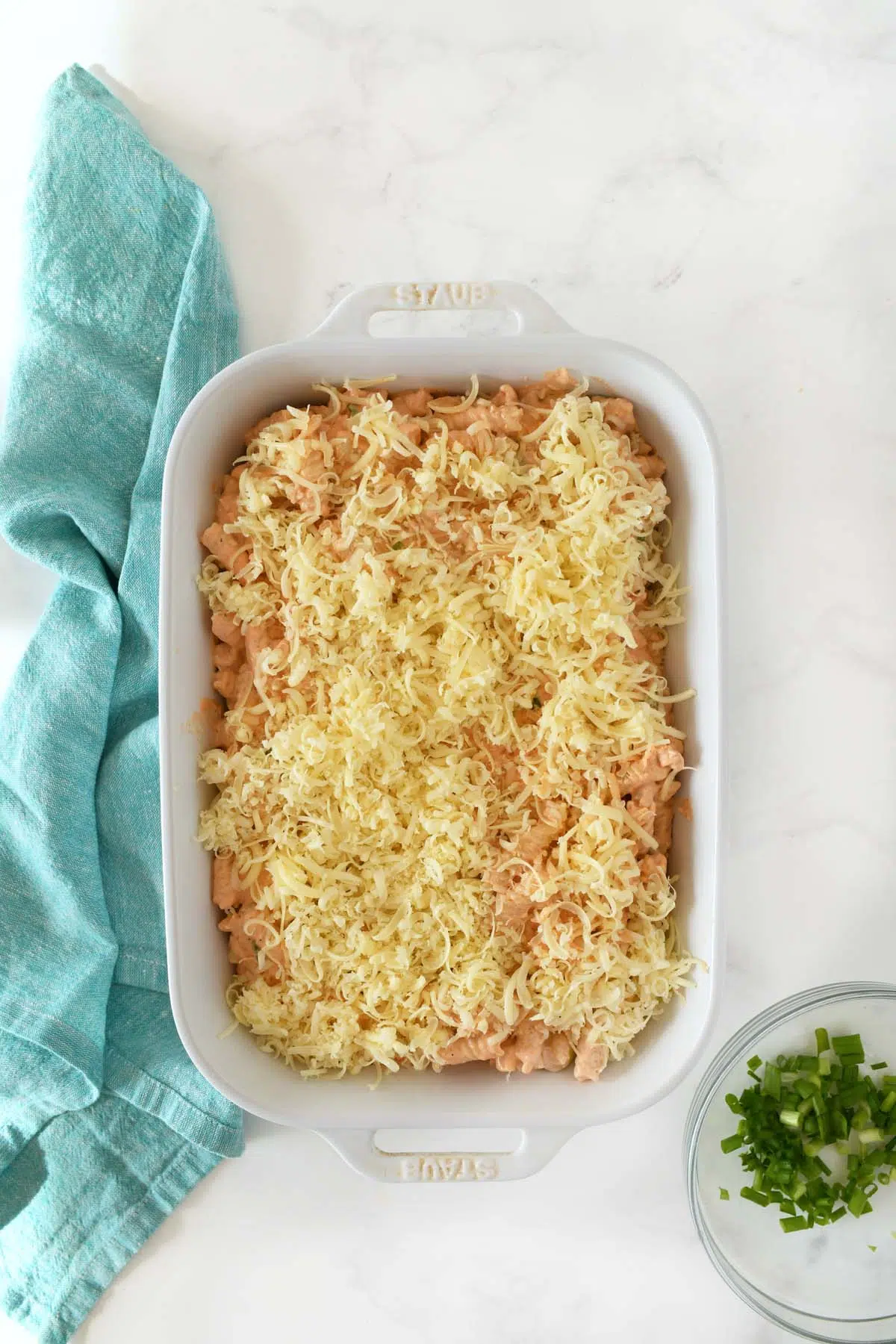 Unbaked buffalo chicken pasta in a white dish with a blue napkin.
