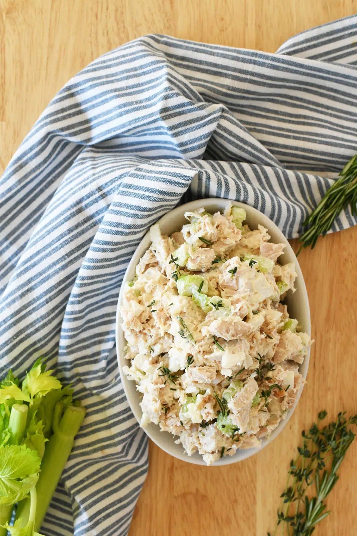 Turkey salad in a white dish near a blue, striped napkin with green celery and herbs.