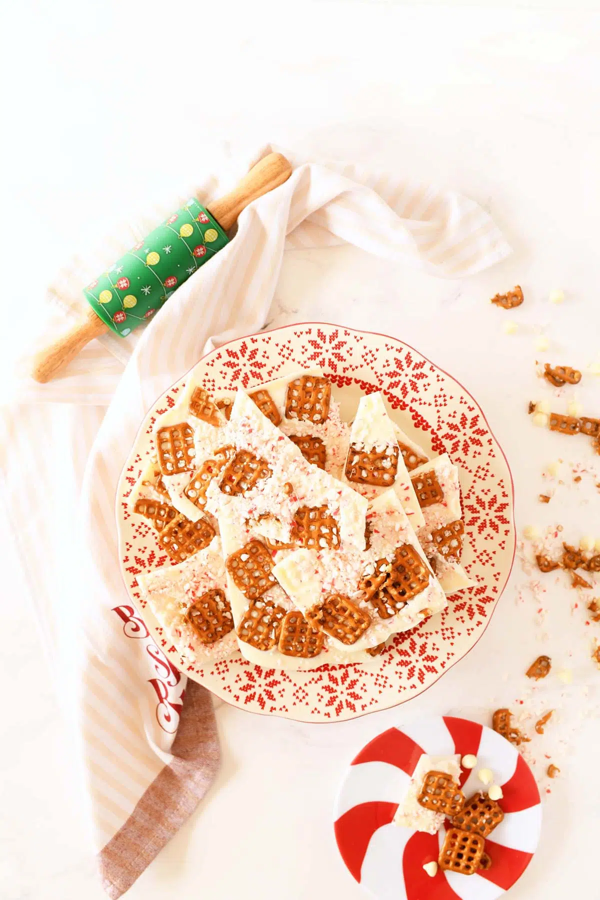 White chocolate mint pretzel bark on a white table with a red peppermint plate nearby.