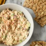 Chicken salad in a white bowl with crackers and a yellow towel.