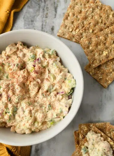 Chicken salad in a white bowl with crackers and a yellow towel.