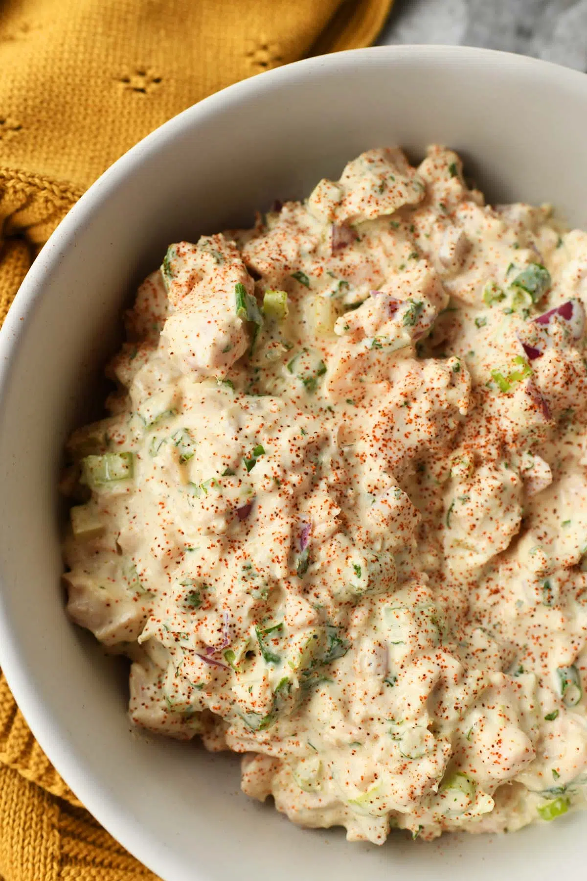 Up close shot of chicken salad ingredients in a white bowl with a yellow napkin nearby.
