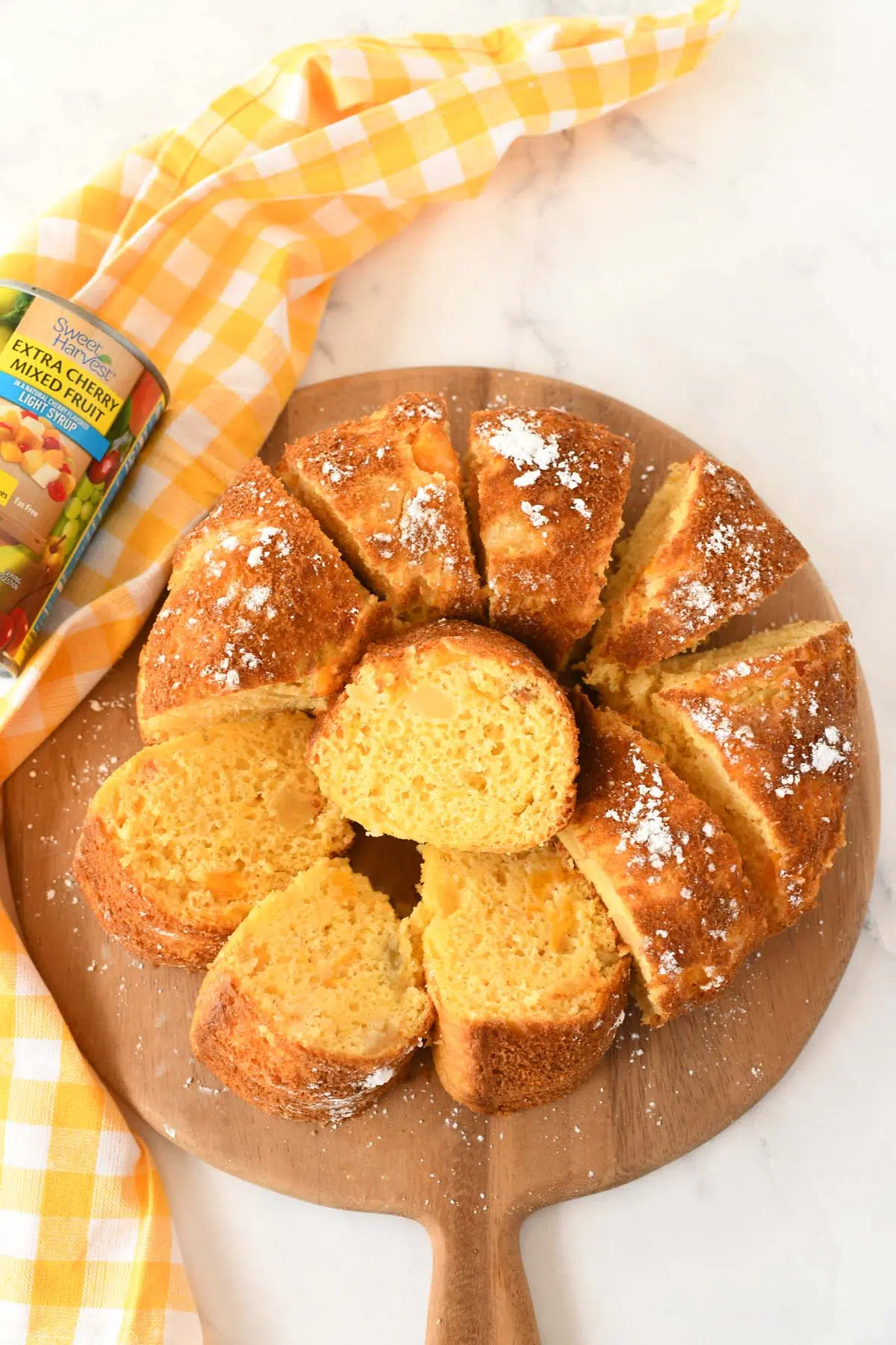 Sliced golden brown bundt cake on a wooden server with a yellow napkin nearby.