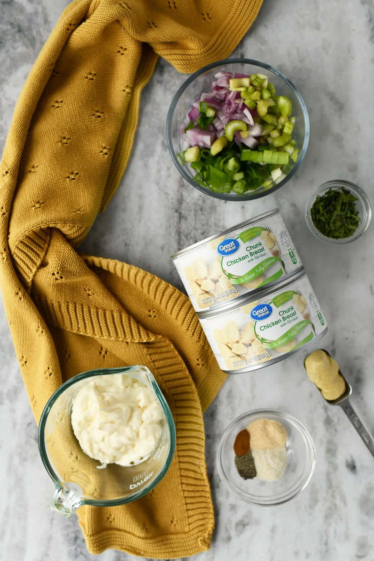 Cans of chicken salad and ingredients on a stone table with a yellow towel.