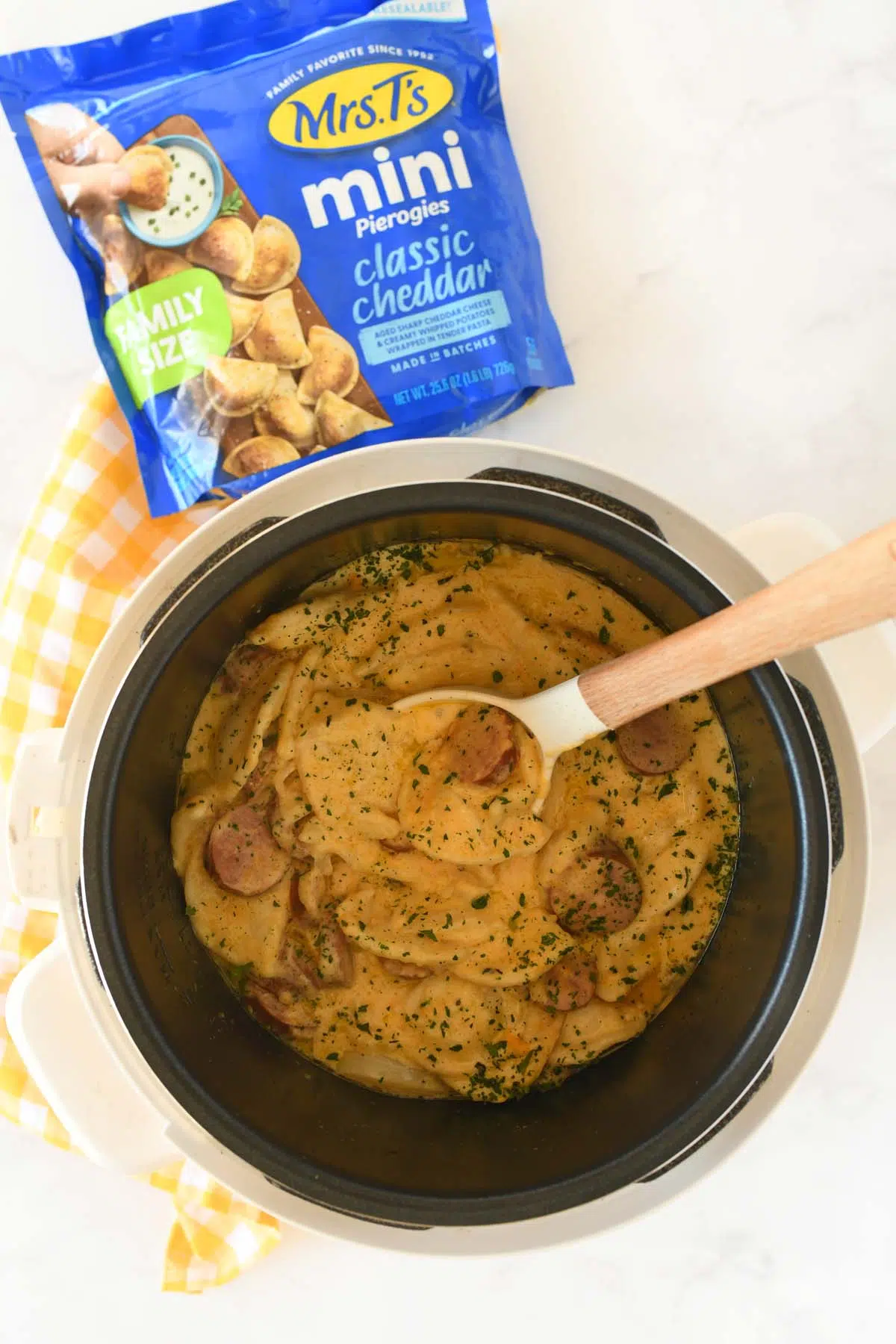 Pierogi casserole in a slow cooker. A blue bag of Mrs. T's Pierogis and a yellow napkin is nearby.