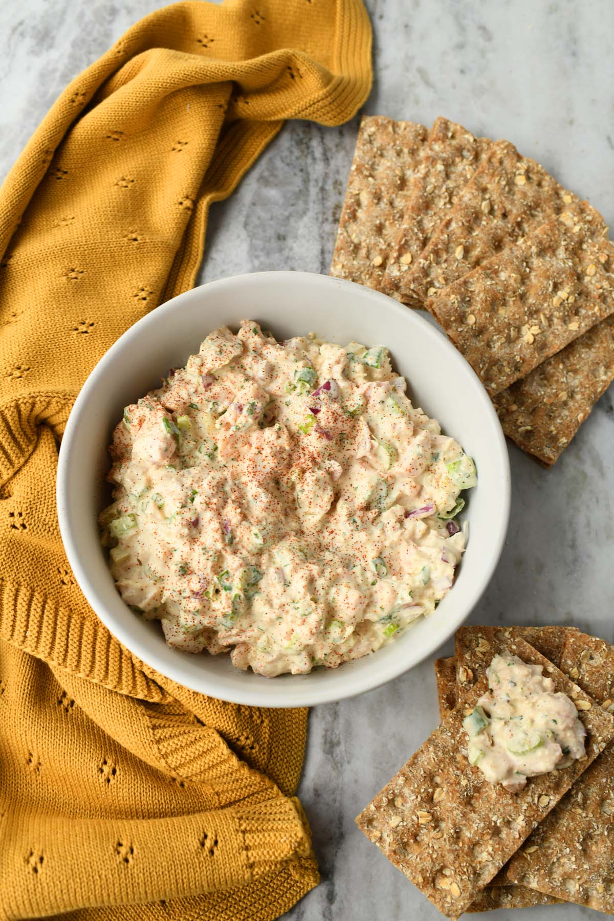 Canned chicken salad in a white bowl near a yellow towel, and rectangle-shaped crackers.