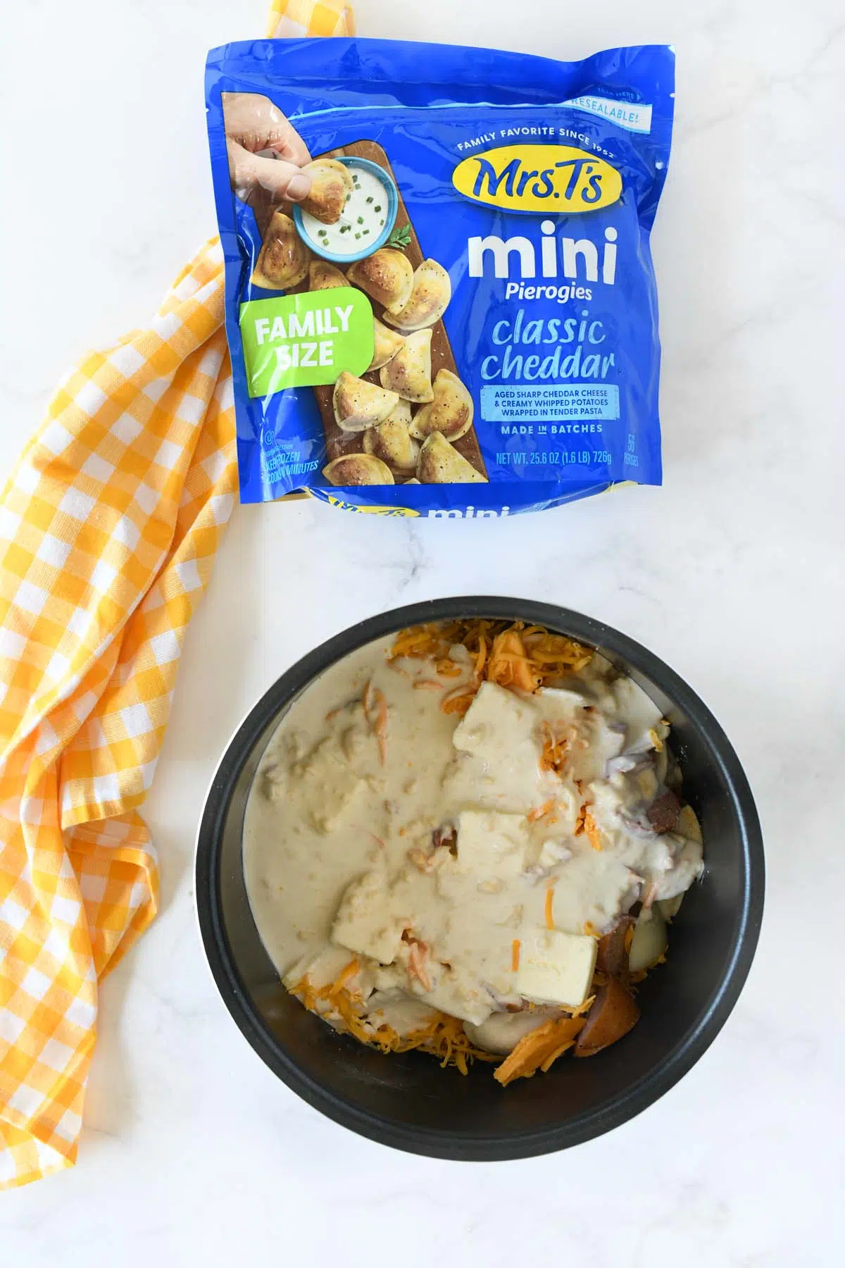 Creamy mixture in a slow cooker insert near a blue bag of Mrs. T's Pierogis and a yellow napkin.