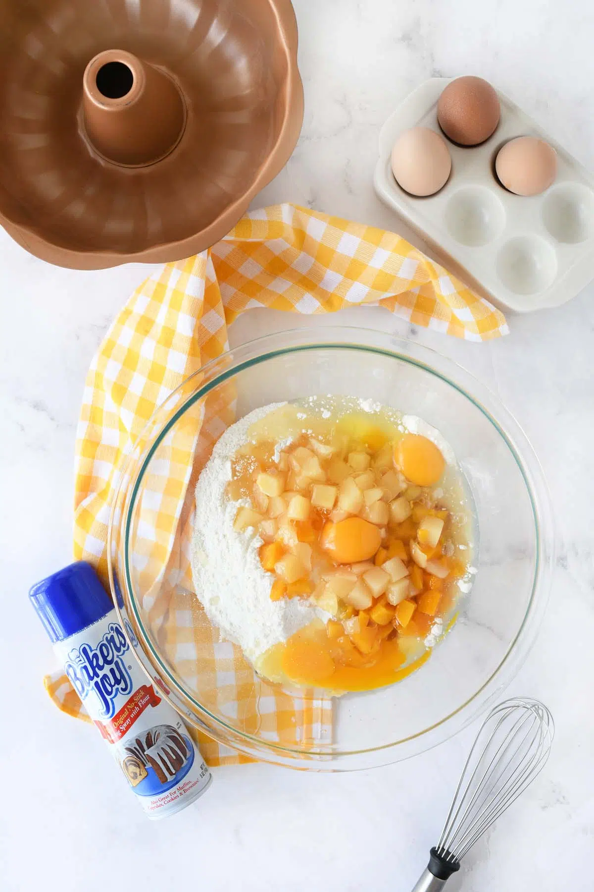 Fruit cocktail cake batter in a glass bowl with a copper cake pan, and nonstick spray nearby.