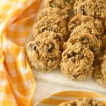 A platter of cowboy cookies on a white tray near a yellow, checkered napkin.