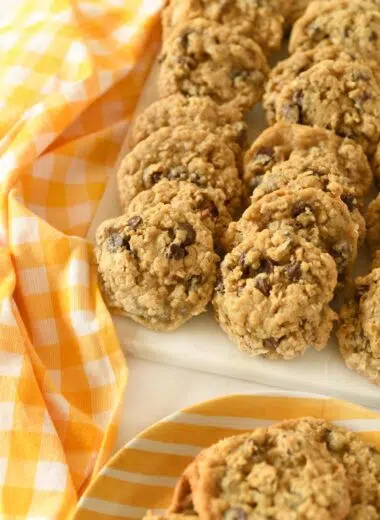 A platter of cowboy cookies on a white tray near a yellow, checkered napkin.