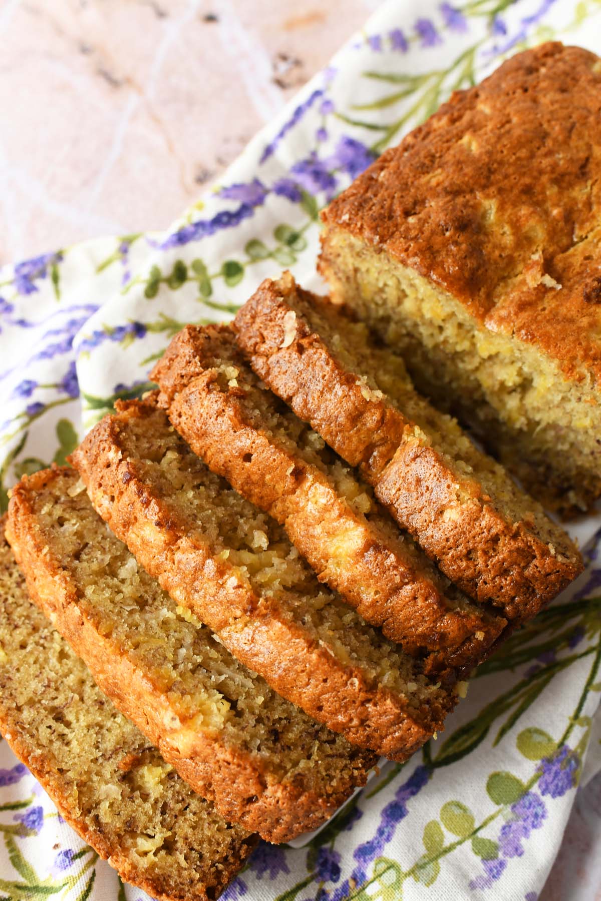 Slices of banana pineapple bread near a purple, floral napkin.