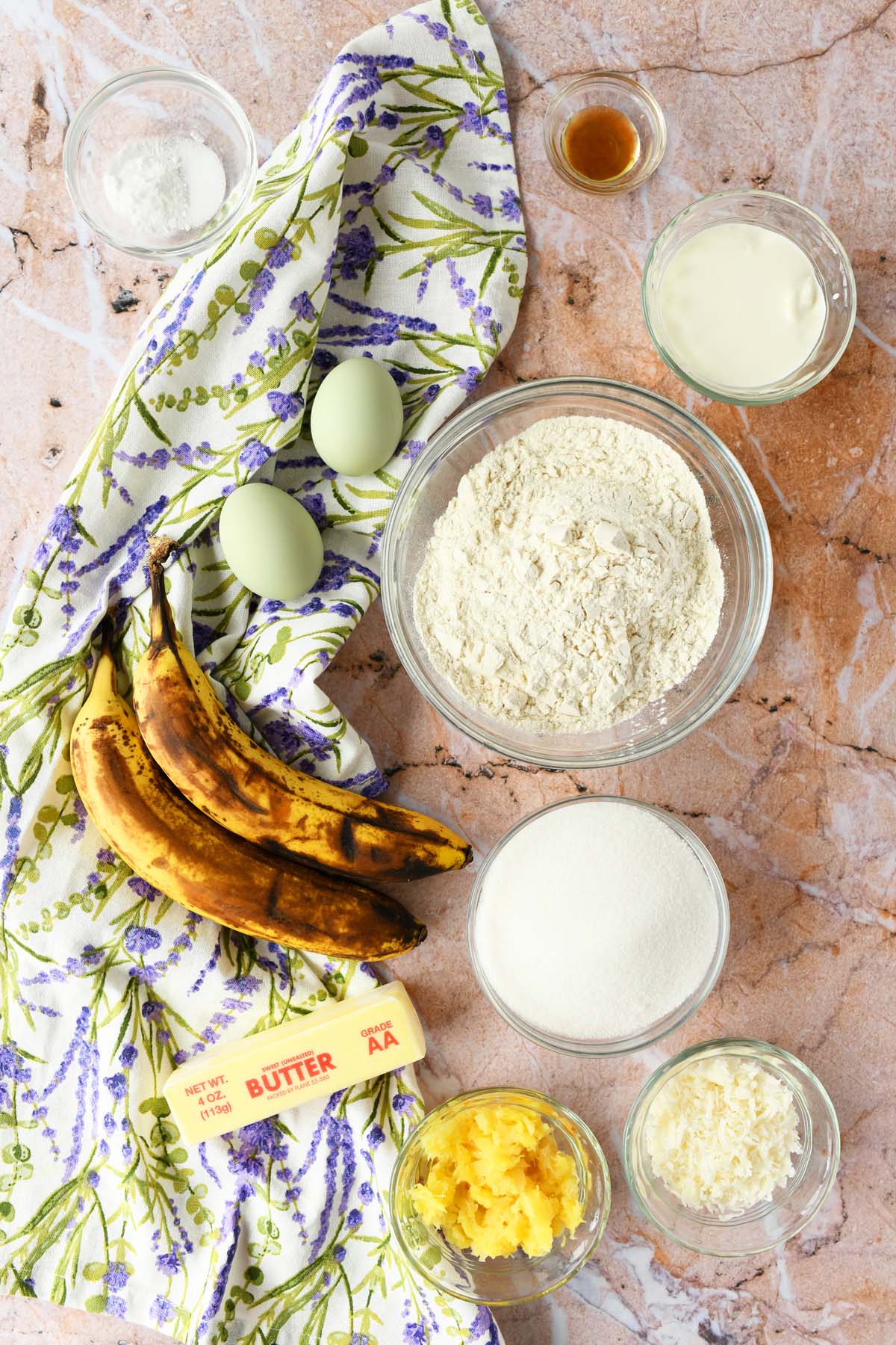 Pineapple Banana Bread ingredients on a tan, marble table with a floral, purple napkin.