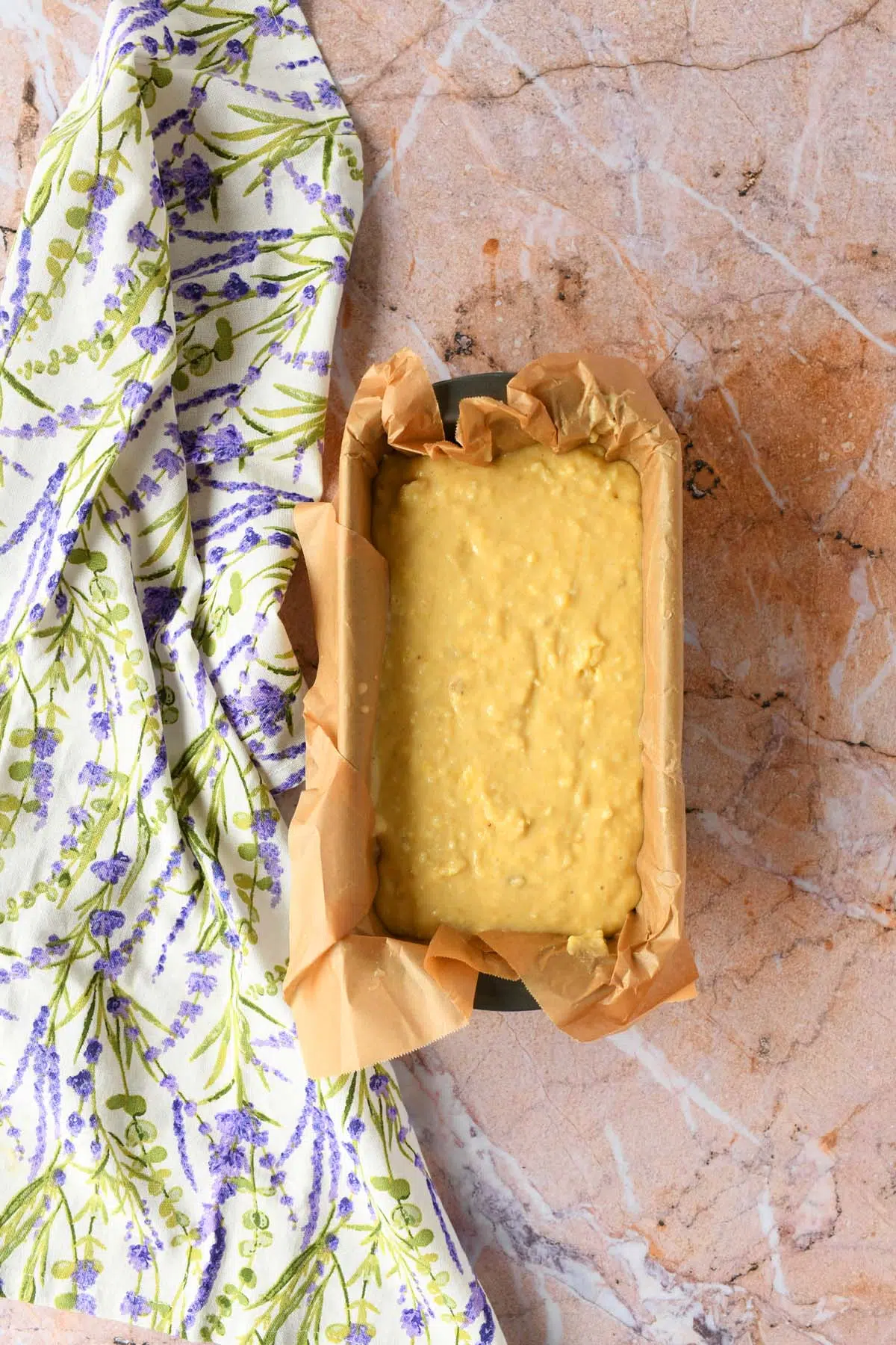 Pineapple banana bread batter in a loaf pan with a purple floral napkin nearby.
