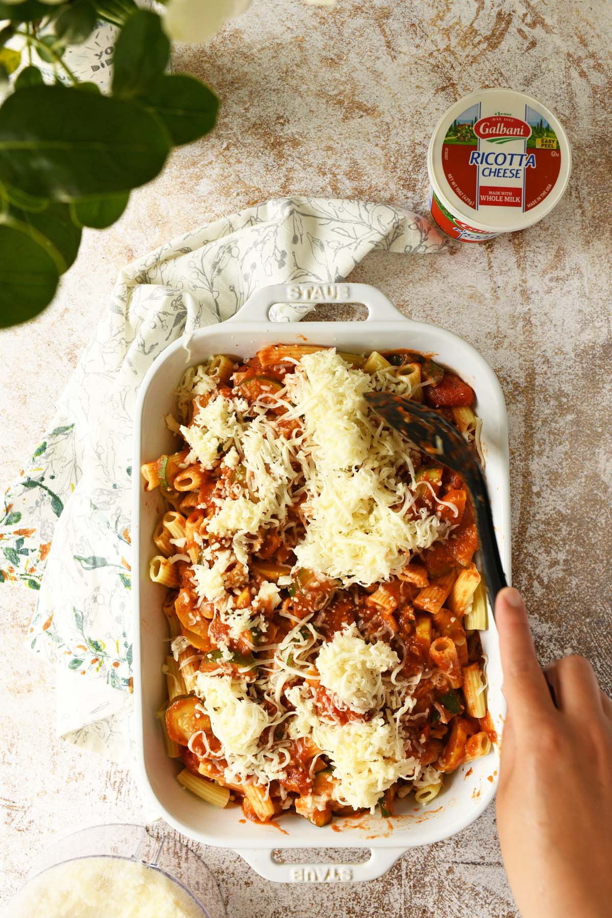 A hand mixing in mozzarella cheese to baked ziti.