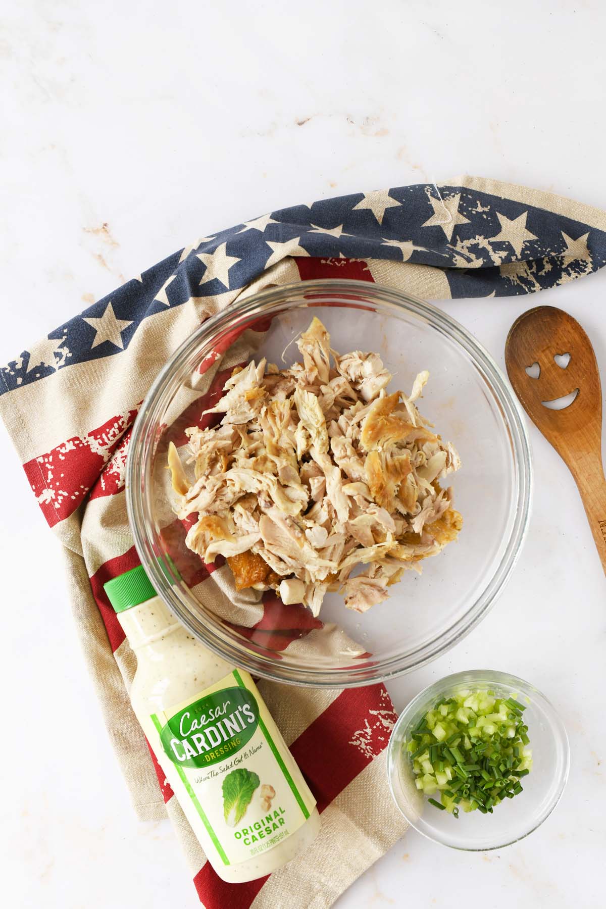 Shredded chicken in a bowl near a bottle of caesar salad dressing and a patriotic napkin.