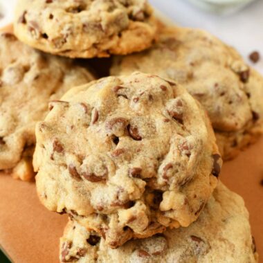 An upclose shot of thick chocolate chips cookies stacked on brown parchment paper.