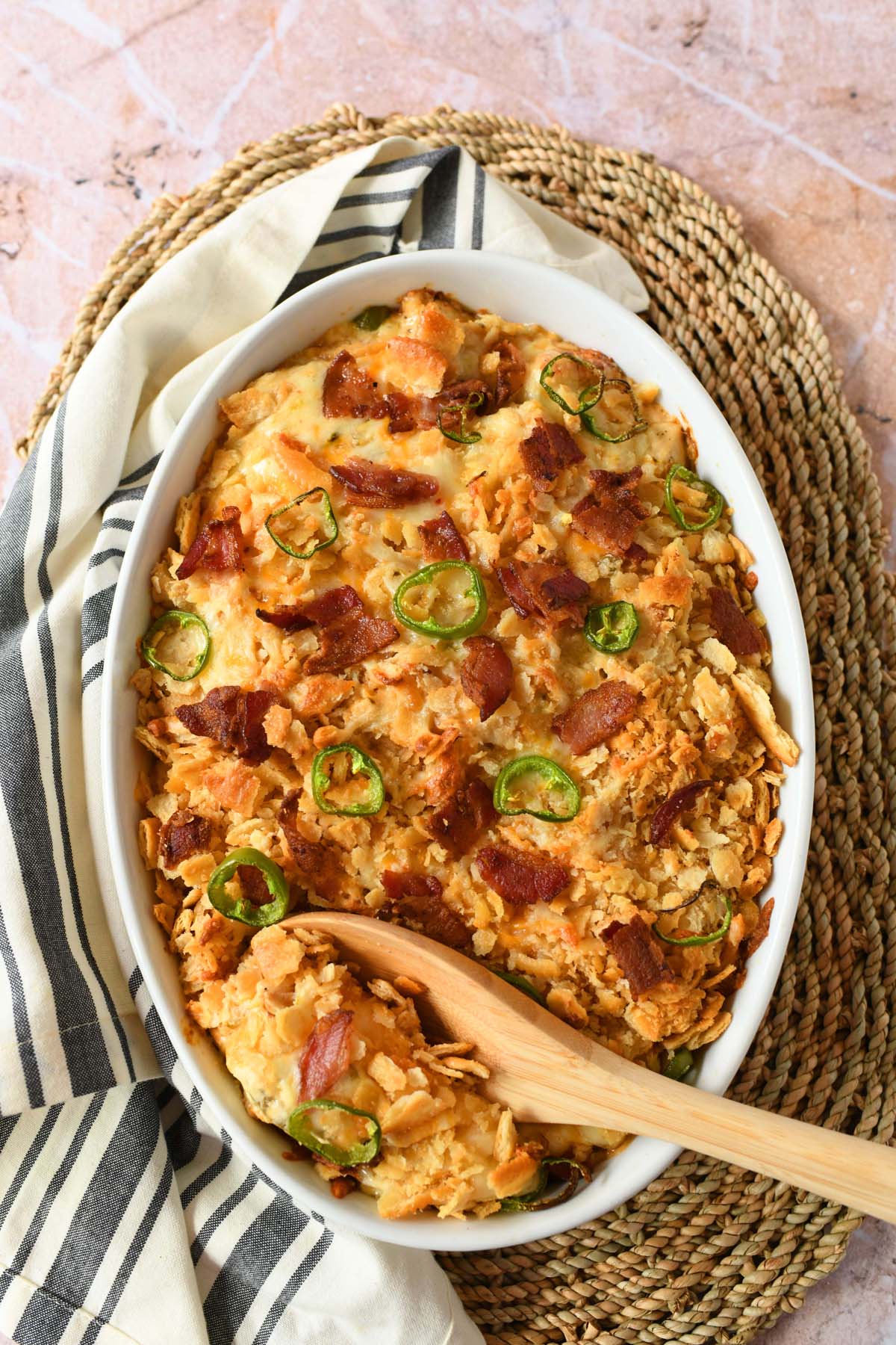 A wooden spoon with jalapeno popper casserole in white baker.