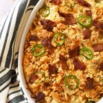 Cheesy chicken jalapeno popper bake in a white oval baker near a striped napkin.