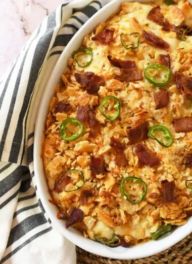 Cheesy chicken jalapeno popper bake in a white oval baker near a striped napkin.