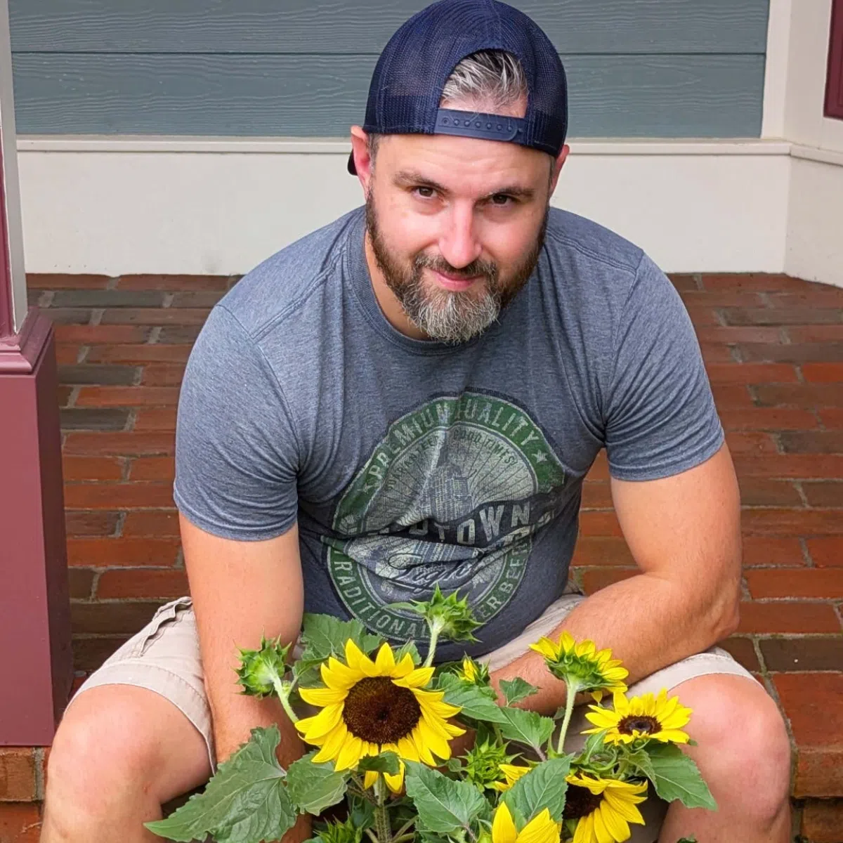 A man outdoors on a brick porch with yellow sunflowers.