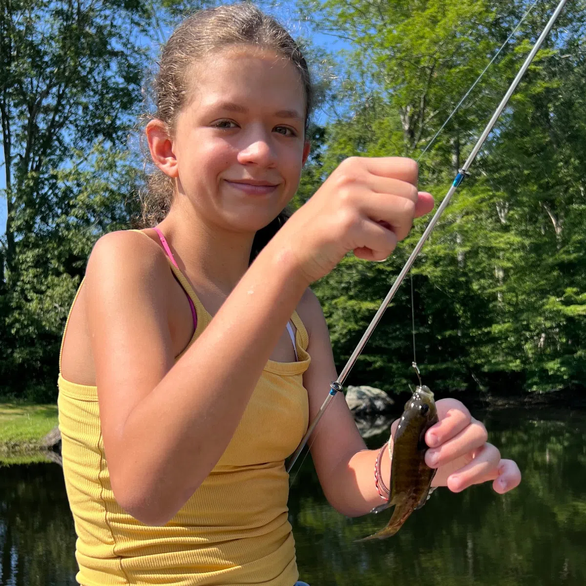 Girl in a yellow shirt with a fish on a rod.