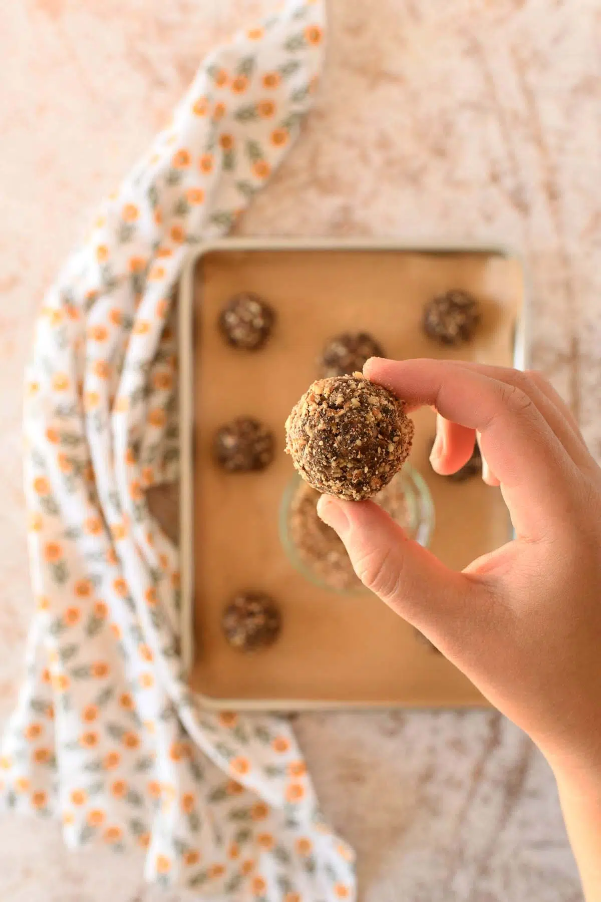 A hand holding up a pecan crusted energy ball.